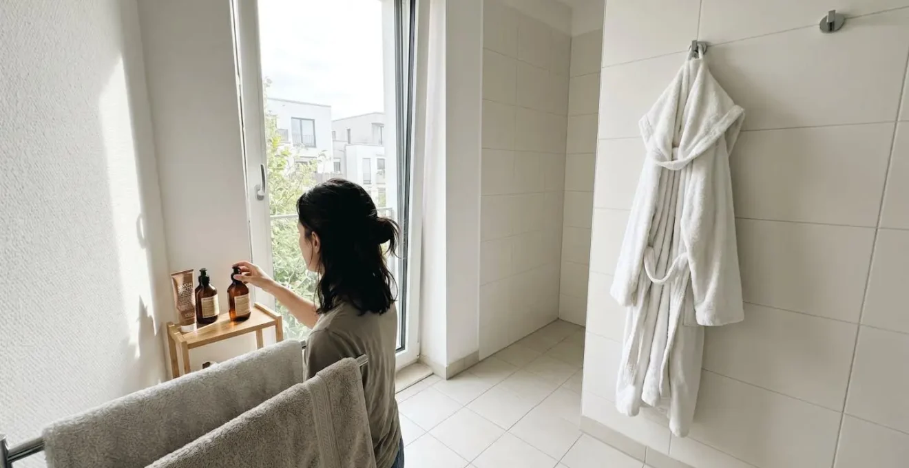Étiquette textile d'un peignoir blanc suspendu montrant composition et grammage dans une salle de bain moderne lumineuse